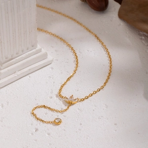 Collier en Y doré avec zircons en forme de pétales sur surface en marbre blanc