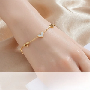 Detailed close-up of gold chain bracelet featuring shell heart charms on a wrist