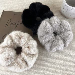 Detailed view of plush faux fur scrunchies in black, grey, and beige on a cozy knit fabric