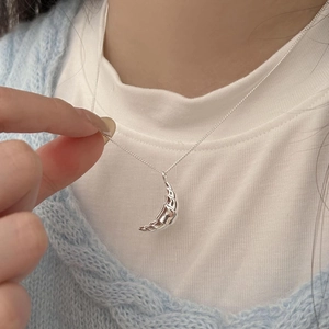 Close-up of polished silver croissant pendant necklace worn on a soft knit cardigan
