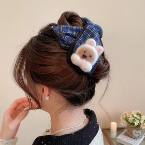 Detail view of blue plaid hair claw clip with plush cartoon decor worn on long hair