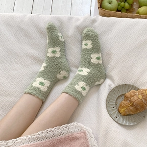 Close-up of thick sage green coral fleece socks with white floral patterns in a cozy setting