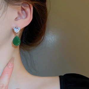 Close-up of heart zircon and green teardrop gemstone earrings worn by a model