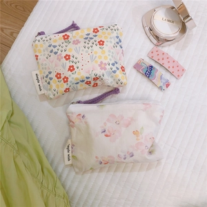 Close-up of floral cotton mini pouches with zipper and woven labels on a white quilted mat