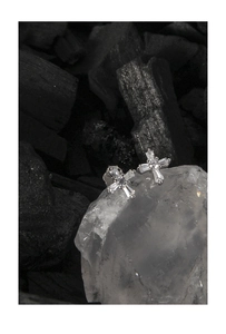Macro shot of silver cross stud earrings with sparkling stones on textured stones