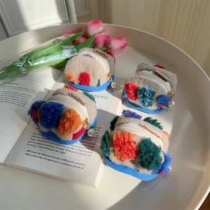 Set of beige plush bucket purses with colorful pom-poms on a white tray with tulips