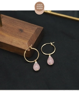 Macro detail of gold hoop earrings with pink crystal drop and white pearl accent