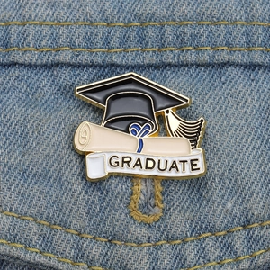 Close-up of a graduate cap enamel pin with golden tassel pinned on blue denim fabric