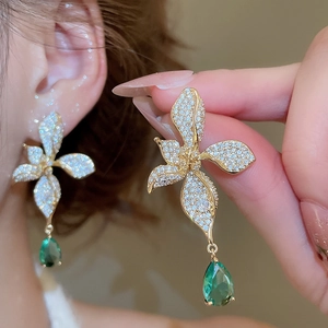 Detailed macro view of gold plated flower earrings with cubic zirconia and green teardrop gem