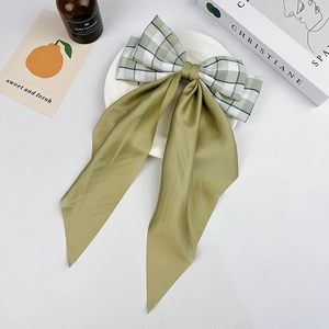 Detailed view of a green plaid bow hair clip with long ribbons on a clean background