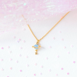 Detailed close-up of a golden planet pendant with a blue stone and star on pink tulle