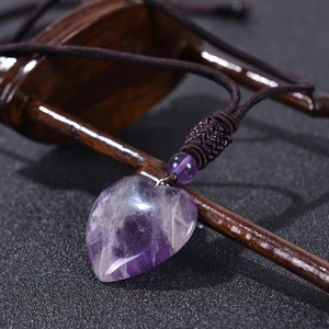 Detailed view of heart-shaped amethyst pendant with brown braided rope on wooden stand