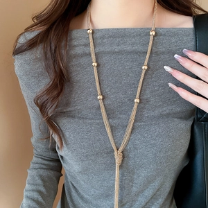 Detail of layered gold chain necklace with metallic beads and a knotted tassel design