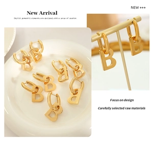 Close-up of gold-plated B-shaped geometric drop earrings on display stand and tray