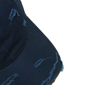 Macro detail of distressed navy blue cotton baseball cap showing ripped edges and texture