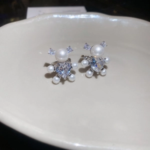 Close-up of bear-shaped earrings with heart zircon and white pearls on a white plate