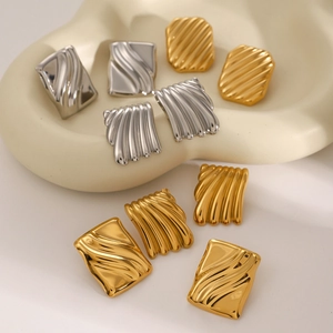 Square wavy textured earrings in gold and silver finish on a ceramic tray