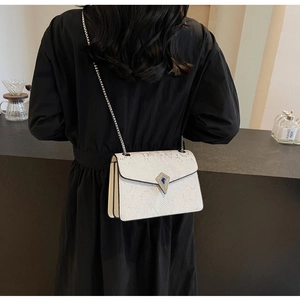 Detailed shot of a white snakeskin chain bag with a blue gemstone diamond buckle