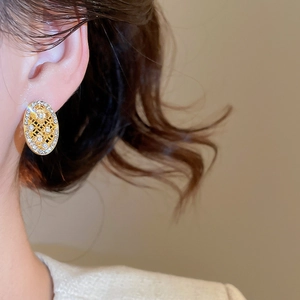 Dettaglio di orecchini ovali cavi dorati con strass indossati sulla modella