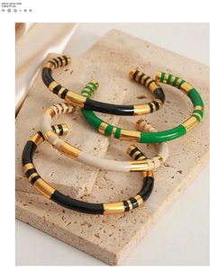 Detail of striped enamel gold-plated bangles in green and white on a stone pedestal