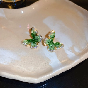 Détail de boucles d'oreilles papillon dorées serties de cristaux verts et de zircons