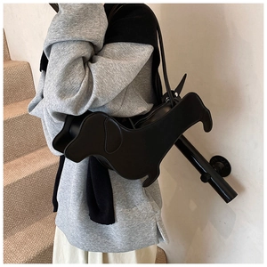 Side view of a black dachshund-shaped leather tote bag worn as an underarm shoulder bag