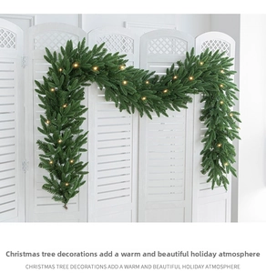 Close-up of green Christmas garland with warm yellow LED lights on white background