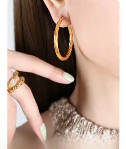 Macro detail of large gold twisted hoop earrings and textured hammer finish metal rings
