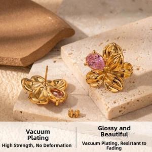 Macro shot of gold floral earrings with pink teardrop crystal on textured stone
