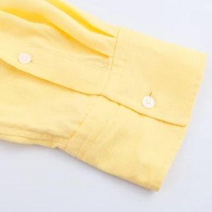 Détail de la manchette d'une chemise en lin jaune avec bouton blanc et couture