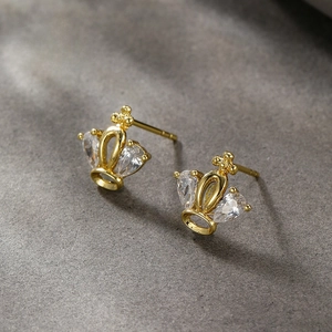 Detail shot of 14K gold-plated crown stud earrings with water-drop zircons on stone surface