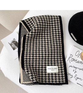 Detailed view of knitted houndstooth scarf with black and cream pattern on soft surface