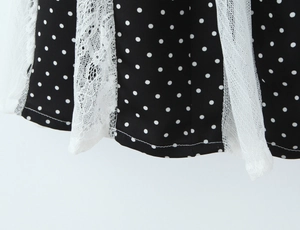 Detailed view of the black polka dot fabric with white lace trim and sheer mesh hem