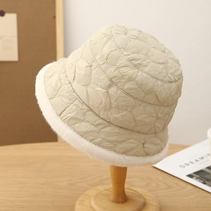 Minimalist beige quilted bucket hat with faux fur brim on a wooden stand