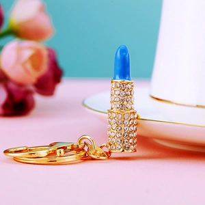 Close-up of a blue and gold crystal-encrusted lipstick keychain with a large lobster clasp