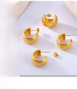 Detailed view of four golden C-shaped wave earrings on white textured leather background