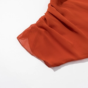 Close-up of pleated orange-red chiffon fabric showing texture and hemline craftsmanship