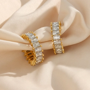 Détail macro de boucles d'oreilles C en or 18K avec zircons rectangulaires sur soie beige