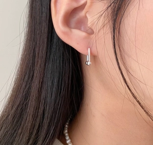 Close-up of minimalist silver U-shaped stud earrings worn with a pearl necklace