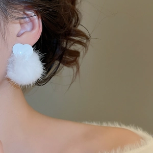 Detail of white heart-shaped stud earring with fluffy faux fur pompom for winter