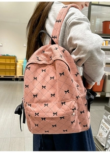 Pink corduroy backpack with black bow prints and ribbon detail shown on model