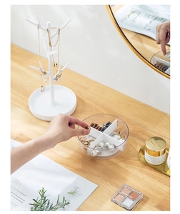 Detail showing a hand picking jewelry from a rotating clear tray and white jewelry tree