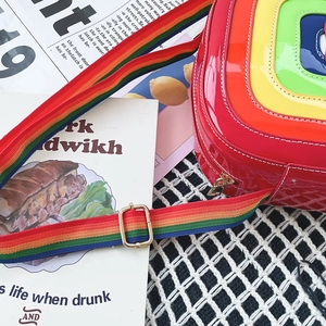 Close-up of rainbow crossbody bag in glossy patent leather with striped fabric strap