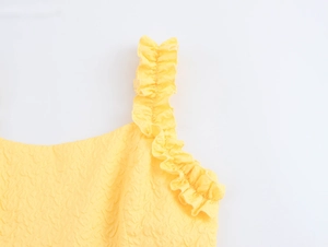 Detailed macro view of yellow ruffled shoulder straps and embossed fabric texture on dress