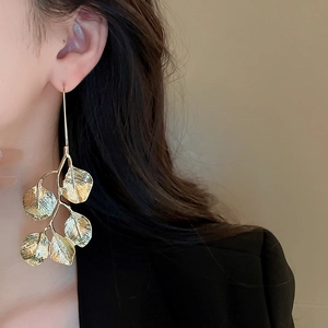Close-up of golden leaf earrings on a model showing detailed branch textures and metallic finish
