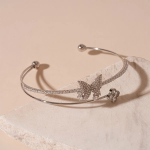Detail of silver double-layered bracelet with zircon butterfly and clover on white stone