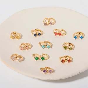 Macro view of gold huggie earrings set with various colored square cut gemstones