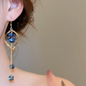 Dettaglio di orecchini geometrici pendenti con cristalli blu e nappe su modella
