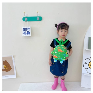 Toddler wearing a bright green dinosaur backpack with cartoon prints in a cozy room