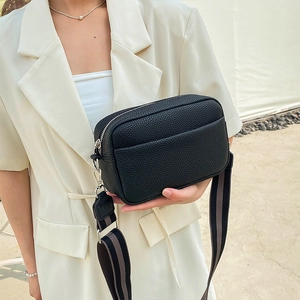 Close-up of black litchi pattern leather cross-body bag with striped fabric wide strap